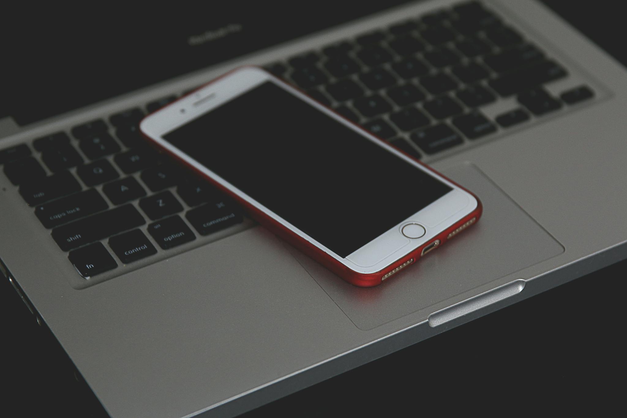 A smartphone with a red case resting on a laptop keyboard, showcasing modern technology indoors.